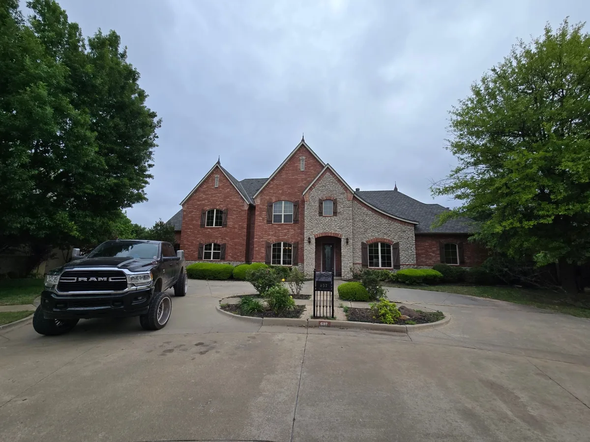 Large brick and stone estate home with a completed roof, work truck parked in the driveway